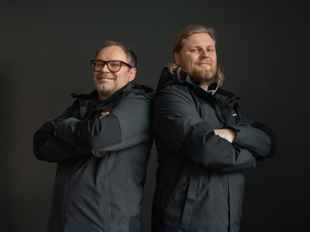 Jesse Salomäki ja Seppo Salomäki poseeraamassa Rinta-Jouppi Machinen työvaatteissa mustaa taustaa vasten